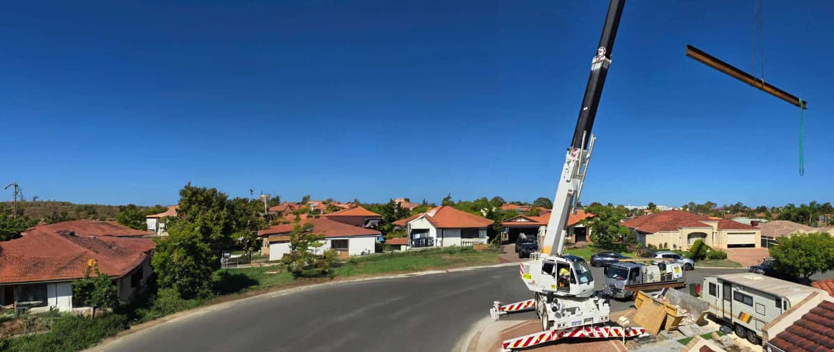 Crane lifting load-bearing beam into residential property.